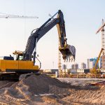 Yellow excavator operating on active construction site — heavy plant equipment subject to pre-use inspection requirements under PUWER