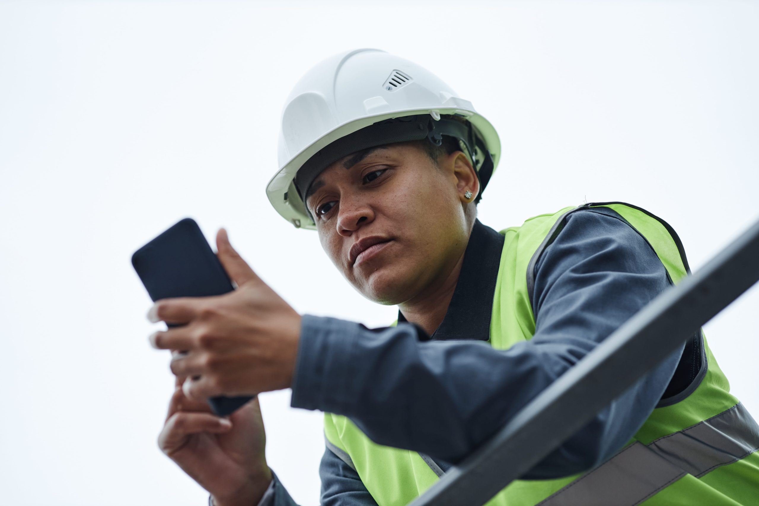 Construction site worker in hard hat using smartphone to complete a pre-use inspection software checklist on site