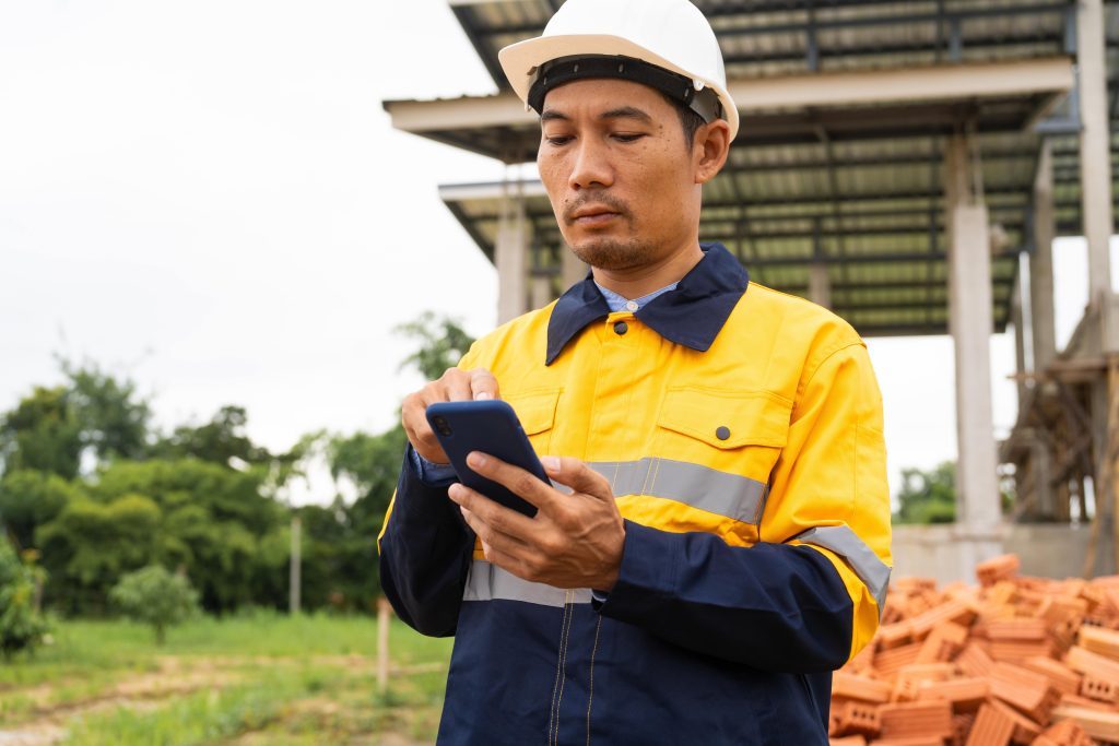 Construction worker in hi-vis completing a digital pre-use inspection checklist on a smartphone on site